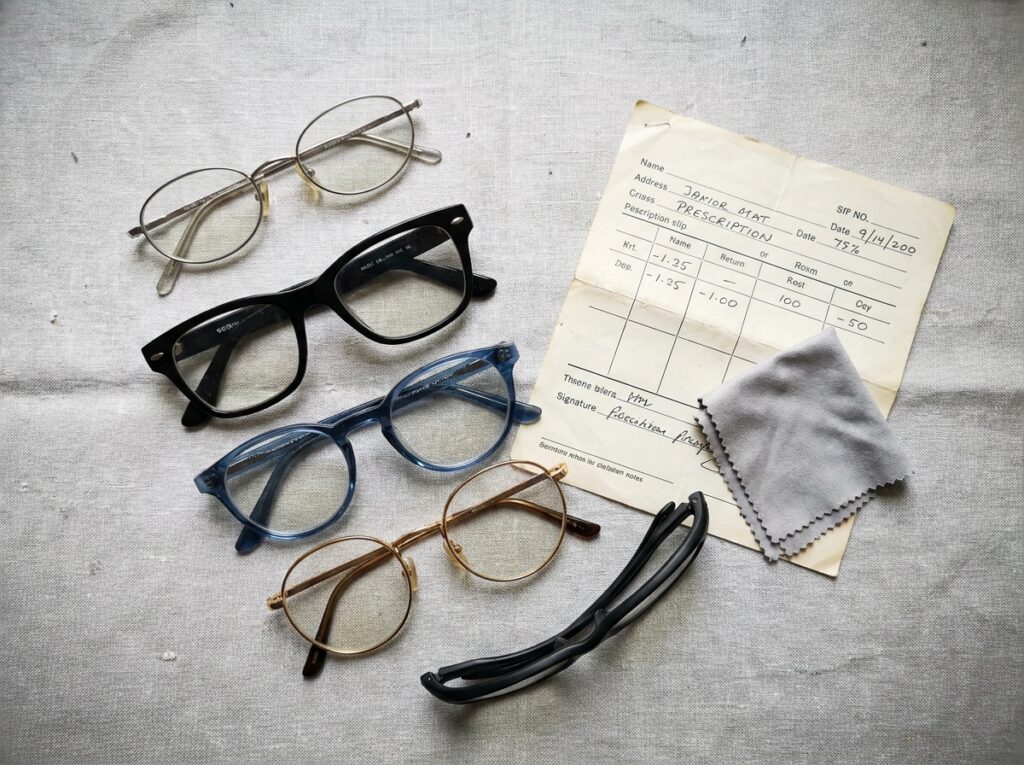 Sélection de cinq montures de lunettes différentes présentées en flat lay sur fond gris texturé